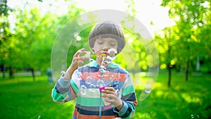 Close up portrait of happy little cute boy blowing, having fun with soap bubbles in park. Little child playing outside