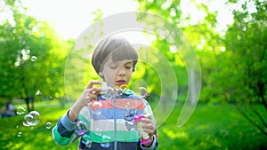 Close up portrait of happy little cute boy blowing, having fun with soap bubbles in park. Little child playing outside