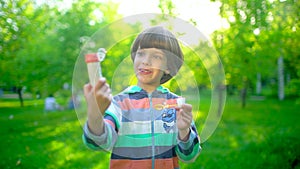 Close up portrait of happy little cute boy blowing, having fun with soap bubbles in park. Little child playing outside