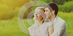 Close up portrait of happy lovely young couple sitting on the grass together looking away over green summer background