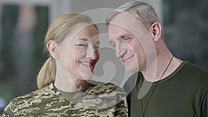Close-up portrait of happy loving female soldier and smiling man looking at each other, turning to camera and smiling