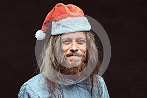 Close-up portrait of a happy male with long hair and beard in blue shirt and red Santa hat.