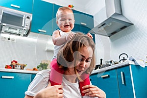 Close-up portrait of a happy mother and her baby sitting on her shoulders. The kitchen is in the background. Bottom view. The