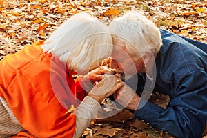 Close up portrait of a happy old man kissing his wife`s hands. In the park in autumn foliage a happy couple is resting