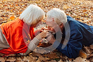 Close up portrait of a happy old man kissing his wife`s hands. In the park in autumn foliage a happy couple is resting