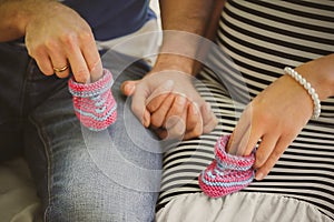 Close up portrait of happy pregnant woman together with husband holding small baby shoes, hugging in summer park