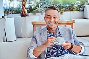 Close-up portrait of a happy rich stylish man dressed in modern elegant clothes holds a cup of coffee at the outdoor