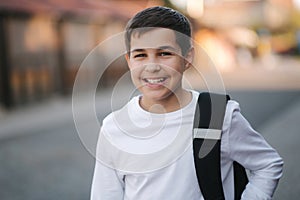 Close up portrait of happy smiled teenage boy in white sweatshirt with backpack outside