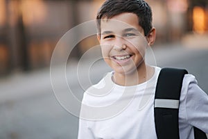 Close up portrait of happy smiled teenage boy in white sweatshirt with backpack outside