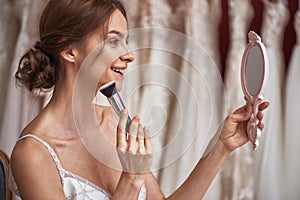 Cheerful bride in wedding dress doing make-up