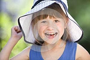 Close-up portrait of happy smiling little girl in a big hat. Child having fun time outdoors in summer