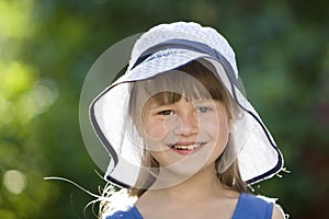 Close-up portrait of happy smiling little girl in a big hat. Child having fun time outdoors in summer
