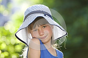 Close-up portrait of happy smiling little girl in a big hat. Child having fun time outdoors in summer