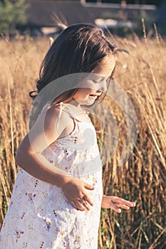 Close-up. Portrait of happy smiling little girl in light sundress made on summer day in field.