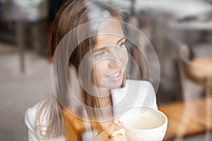 Close-up portrait of happy smiling woman cup of coffee looking through window