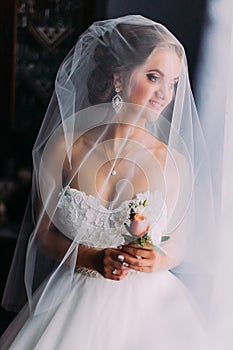 Close up portrait of happy stylish blonde bride in luxury white dress with bouquet under the veil