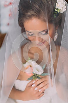 Close up portrait of happy stylish blonde bride in luxury white dress with bouquet under the veil