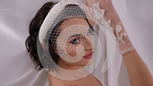 A close-up portrait of a happy sweet bride in transparent lace gloves and a veil