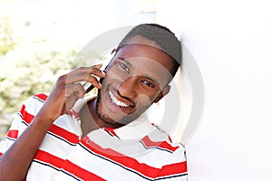 Happy young man leaning to wall and talking on cell phone