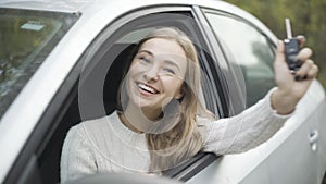 Close-up portrait of happy young beautiful Caucasian woman bragging car keys sitting on driver`s seat. Joyful smiling