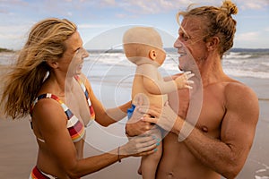 Close up portrait of happy young Caucasian family. Father smiling holding baby boy. Happy mother smiling. Family time on the beach
