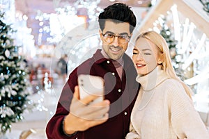Close-up portrait of happy young couple taking selfie picture on mobile phone standing in hall of celebrate shopping