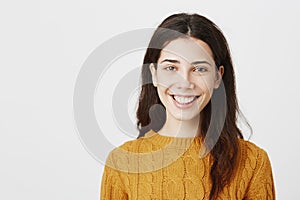 Close-up portrait of happy young european woman smiling broadly wearing yellow sweater and standing over gray background