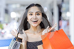 Close-up portrait of a happy young Indian woman standing in a shopping mall, holding paper bags with goods in her hands