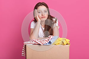 Close up portrait of happy young woman with clothes donation standing over rose background, packing reusable clothes for poor
