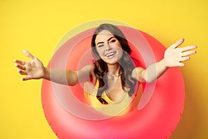 Close up portrait of happy young woman inside pink swimming ring, reaching hands forward, inviting go to the beach