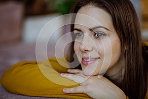 Close-up portrait of happy young woman smiling and looking at camera when restin on sofa at home.