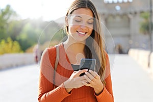 Close up portrait of a happy young woman walking in the city sending text message on cellphone