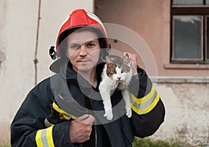 Close-up portrait of heroic fireman in protective suit and red helmet holds saved cat in his arms. Firefighter in fire