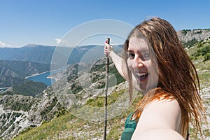 Close up portrait Hiker girl smiling and laughing holding a wood stick. Excursionist red head woman taking a selfie with smart photo