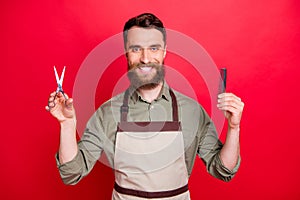 Close-up portrait of his he nice attractive cheerful cheery bearded guy salon owner holding in hands instruments choose