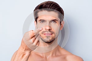 Close-up portrait of his he nice attractive confident bearded brown-haired guy holding on finger invisible eye lens