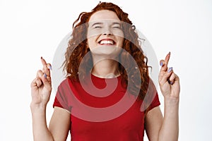 Close up portrait of hopeful and excited woman smiling, standing with fingers crossed and making wish, praying for dream