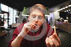 Close-up portrait of a hungry young man eating fries in front of a fast-food restaurant. Student enjoys the taste of french fries