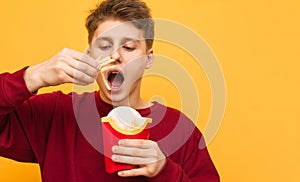 Close up portrait of a hungry young man stands on a yellow background and eats french fries. Guy is eating fast food, isolated.