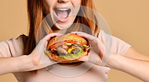 Close up portrait of a hungry young woman eating burger isolated over nude background