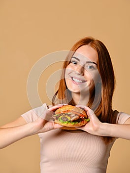 Close up portrait of a hungry young woman eating burger isolated over nude background