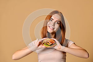 Close up portrait of a hungry young woman eating burger isolated over nude background