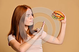 Close up portrait of a hungry young woman eating burger over nude background