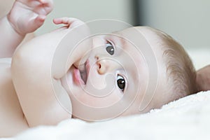 Close up portrait of infant sucking thumb and lying on white bed