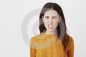 Close-up portrait of irritated mad european woman, grinning and squinting at camera, expressing anger and standing over