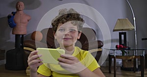 Close-up portrait of joyful Caucasian boy playing video games. Cheerful teenager in yellow T-shirt using smartphone and