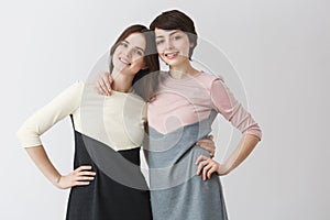 Close up portrait of joyful lesbian couple hugging each other, holding hand on waist, posing for photo in matching