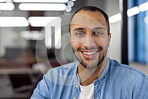 Close-up portrait of a Latin American man sitting in a modern office and smiling at the camera