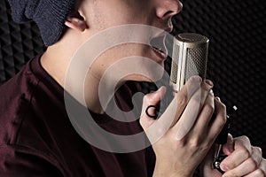 Close-up portrait lips emotional singing the young guy standing in front of the microphone stand holding his hands.