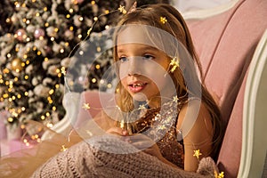 Close up. Portrait of a little beautiful girl framed by the luminous lights of a New Year`s garland. Copy space